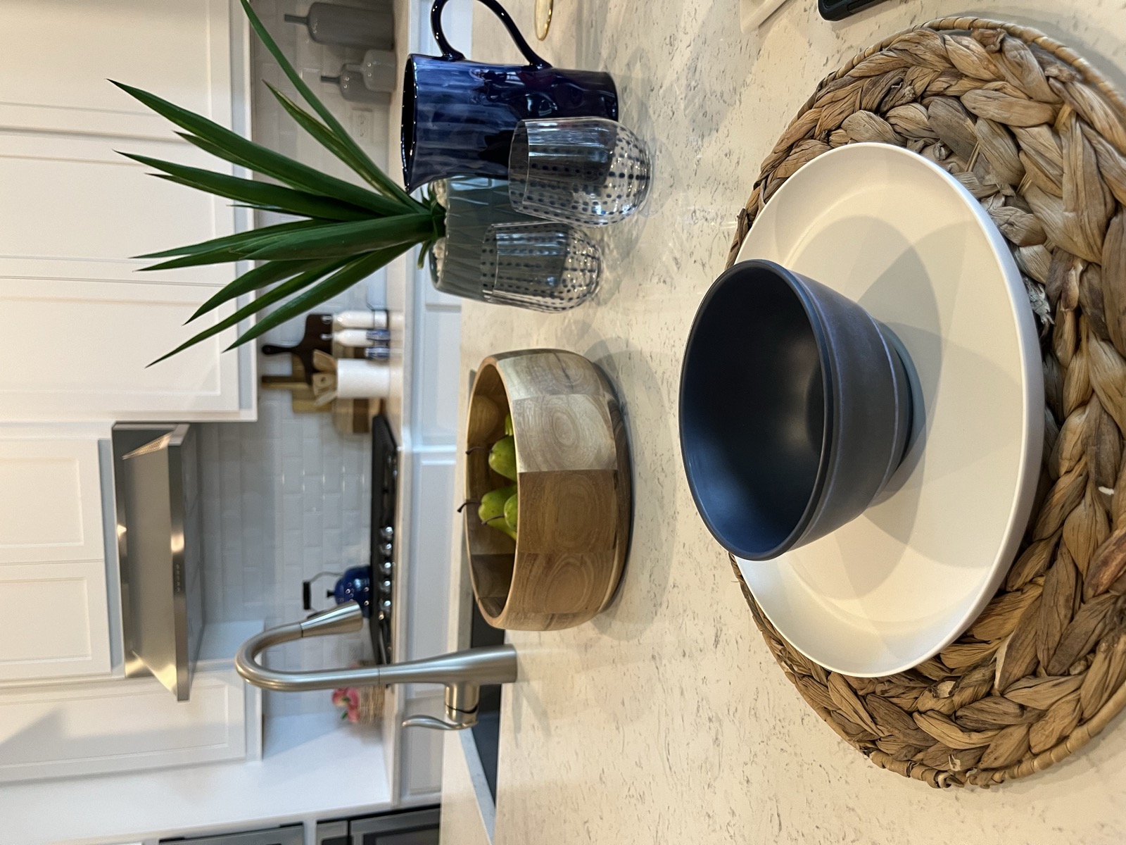 Styled kitchen island place setting with a woven charger, navy bowl, and fresh pears