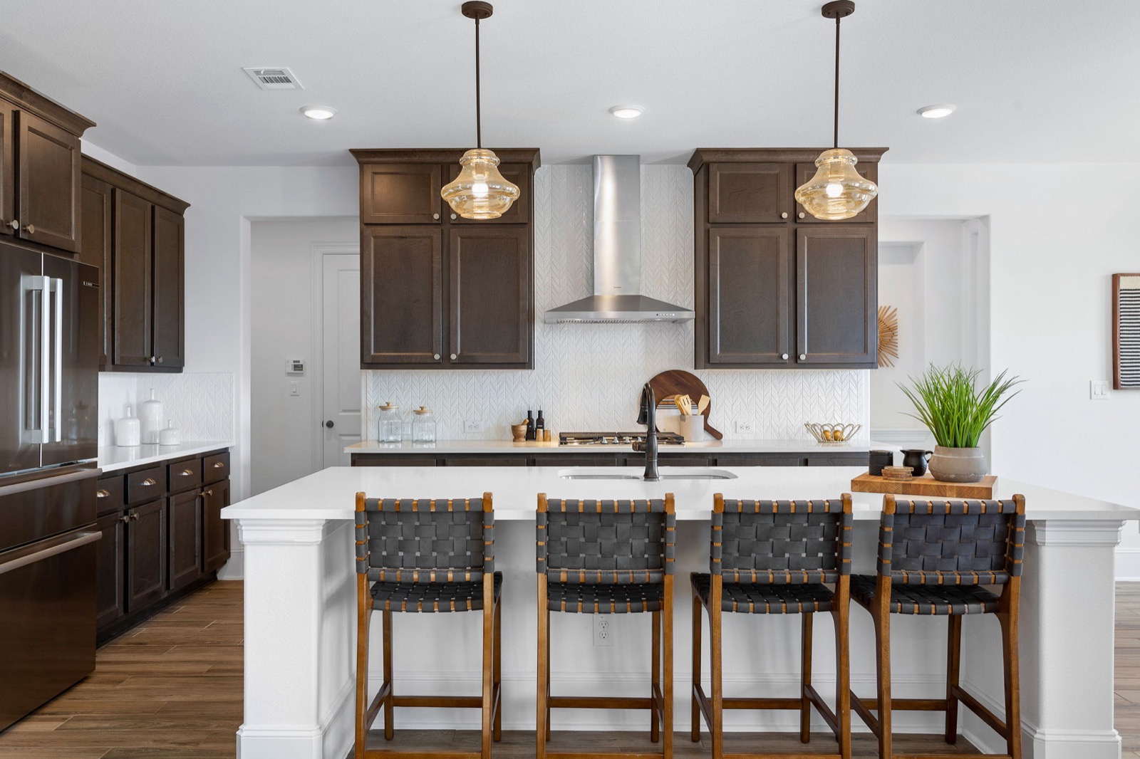 Staged kitchen with dark wood cabinetry, schoolhouse pendants, and woven leather counter stools