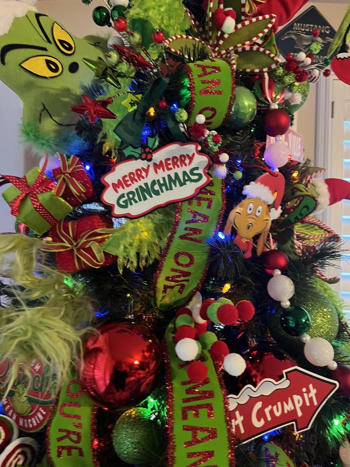 Close-up of a Grinch-themed Christmas tree with a Merry Merry Grinchmas sign, green 'mean one' ribbon, and Whoville character ornaments