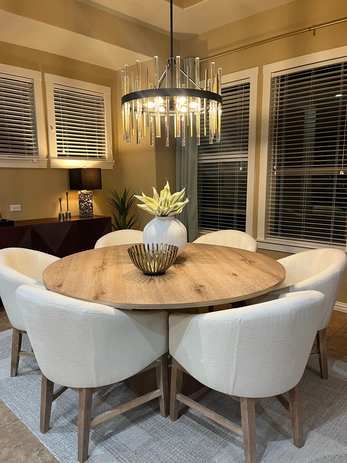 Round oak dining table with cream chairs and modern chandelier
